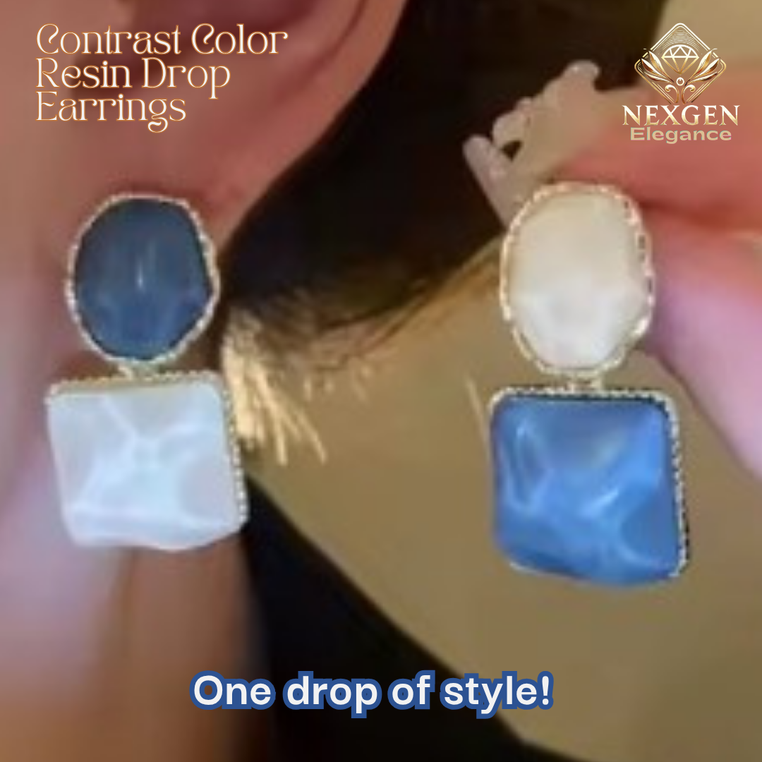A close-up shot of two individual contrast color resin drop earrings. One earring features a blue round resin top with a white square resin bottom, and the other has a white round resin top with a blue square resin bottom. The earrings are set against a blurred background.
