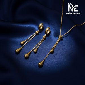 A studio shot of the full Tear Drop Jewelry Set arranged together on a deep blue satin fabric. The photo displays the gold-plated Y-shaped necklace and the coordinating dangling earrings with their tear drop charms.