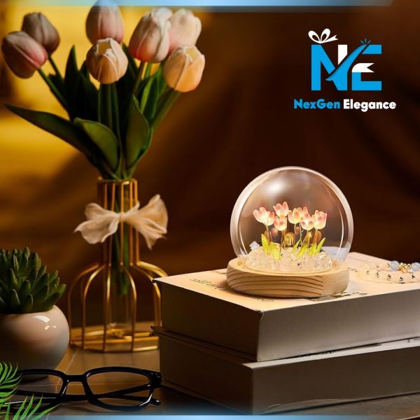 Delicate glowing tulip LED night light in glass dome placed on stack of books beside a gold vase with pink tulips and a small succulent plant.